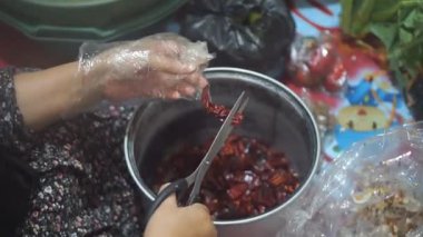 Bir kadının eli kırmızı biberleri makasla temizliyor.