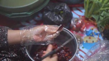 Bir kadının eli kırmızı biberleri makasla temizliyor.