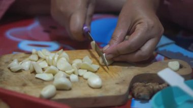 Genç bir kızın eli mutfak bıçağı kullanarak sarımsak doğruyor.