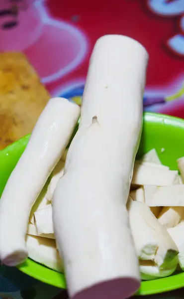 Bir adamın elleri, temiz ve beyaz gözüken bir hayatta kalma bıçağıyla manyok doğrayıp soyar..