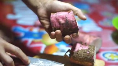 Bir adamın elleri, temiz ve beyaz gözüken bir hayatta kalma bıçağıyla manyok doğrayıp soyar..