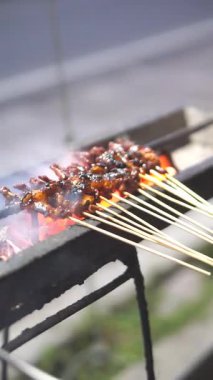 satay being grilled using charcoal with a fan