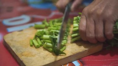 Taze yeşil sebzeleri dilimleyen birinin yakın plan resmi, muhtemelen lahana, tahta kesme tahtasındaki bıçağı kullanarak..