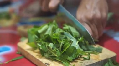 Taze yeşil sebzeleri dilimleyen birinin yakın plan resmi, muhtemelen lahana, tahta kesme tahtasındaki bıçağı kullanarak..