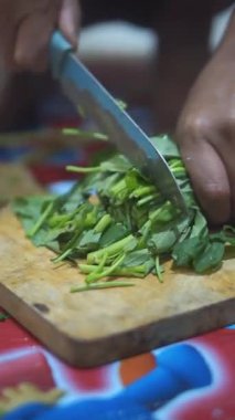 Taze yeşil sebzeleri dilimleyen birinin yakın plan resmi, muhtemelen lahana, tahta kesme tahtasındaki bıçağı kullanarak..