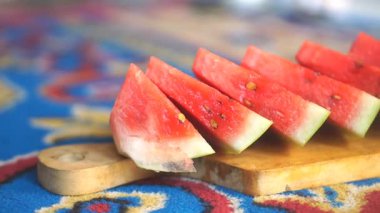 Yakın plan bir el, sulu kırmızı bir karpuzu tahta bir kesme tahtasıyla dilimliyor, tazeliği ve yaz duygusunu vurguluyor..