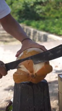  Genç bir hindistancevizini palayla kesen bir adamın yakın plan çekimi. Tropik ortamlarda geleneksel hazırlıkları gösteriyor.