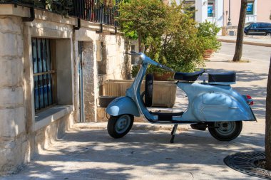 Locorotondo, İtalya. 06 27 19. Vespa marka moped, Aldo Moro Meydanı 'nın gölgesinde kaldırıma park etmiş. İtalya 'da tipik bir geri ulaşım yöntemi.