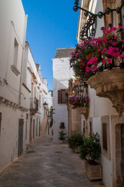 Morelli street and balconies of the Morelli palace in the historic center of Locorotondo, Italy. Colorful doors and windows and potted flowers stand out against the white walls.