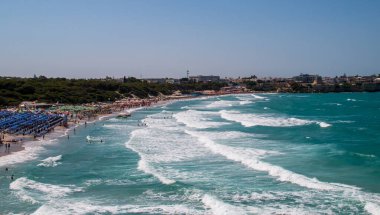 Torre dell'Orso beach in Lecce, Italy. Beach between cliffs crowded with umbrellas and bathers looking to cool off in its warm turquoise waters during the summer.