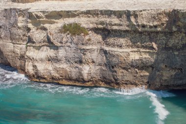 Waves of turquoise water breaking at the foot of a cliff. Rocky limestone beach in Torre dell'Orso, Italy.