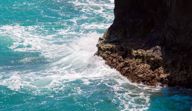 Waves of turquoise water breaking at the foot of a cliff. Rocky limestone beach in Torre dell'Orso, Italy.
