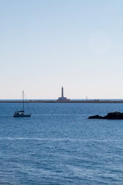 İtalya 'nın Gelibolu kentinden Sant' Andrea adasındaki deniz feneri. Deniz feneri ve diğer adaların yanında yelkenli yelkenliyle ışığa karşı manzara.
