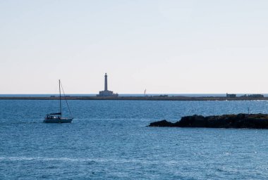 İtalya 'nın Gelibolu kentinden Sant' Andrea adasındaki deniz feneri. Deniz feneri ve diğer adaların yanında yelkenli yelkenliyle ışığa karşı manzara.