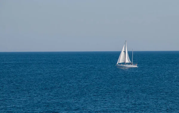 Sailboat sailing on the horizon in Gallipoli, Italy. Yacht with full sails sailing in the turquoise waters of the Ionian Sea.