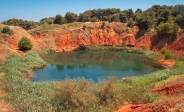 Artificial lake created by flooding an old bauxite quarry in Otranto, Italy. Lagoon surrounded by reeds and with a strong color contrast between the reddish earth and the emerald water. clipart