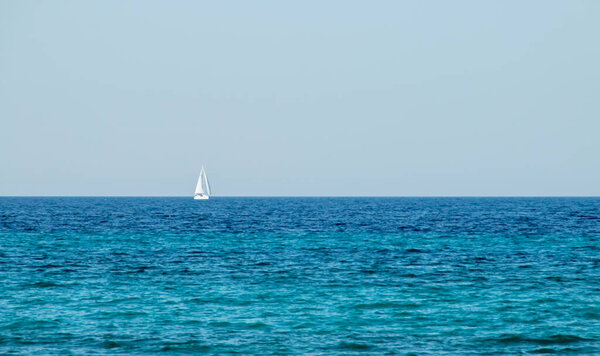 Sailboat sailing on the horizon over a sea of turquoise waters. Otranto, Italy. Sailboat en route through the Otranto channel that connects the Ionian Sea and the Adriatic Sea.