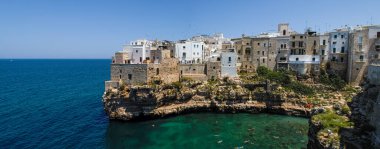 İtalya 'da kireçtaşı uçurumundaki tarihi Polignano a Mare kasabası. Adriyatik Denizi 'ndeki Monachile Koyu' nun güneyinde güneşli bir yaz günü turkuaz suları olan evler..
