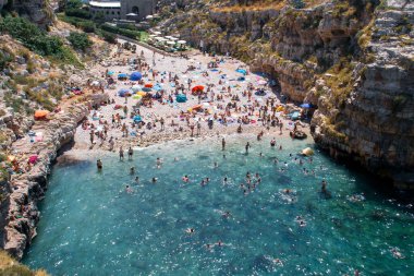 İtalya 'nın tarihi Polignano a Mare kasabasındaki Monachile Koyu. Kireçtaşı kayalıkları arasında küçük bir sahil. Banyo yapan, güneşlenen ya da sıcak bir yaz gününde yüzen..