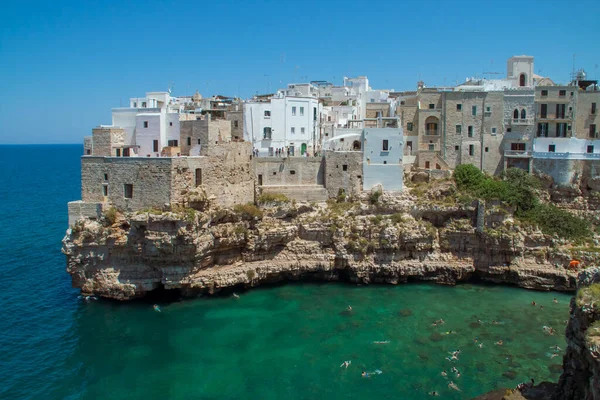 İtalya 'da kireçtaşı uçurumundaki tarihi Polignano a Mare kasabası. Adriyatik Denizi 'ndeki Monachile Koyu' nun güneyinde güneşli bir yaz günü turkuaz suları olan evler..