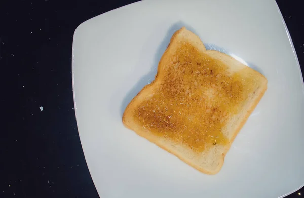 Toast spread with orange marmalade in Madrid, Spain. Toast presented on a white plate.