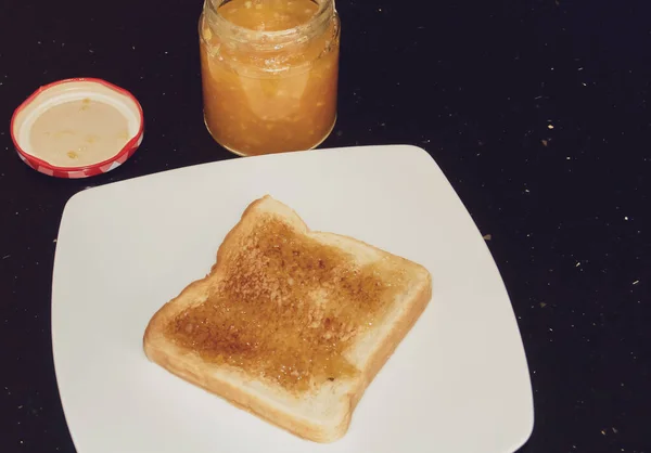 Toast spread with orange marmalade in Madrid, Spain. Toast presented on a white plate next to the glass jar of homemade jam.