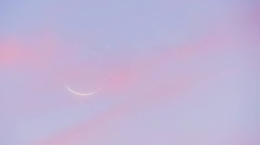 Gün batımında yeni ay. Pembe ve mavimsi tonlarda gökyüzü. Arka planda yeni ayın profili var..
