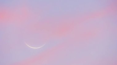 Gün batımında yeni ay. Pembe ve mavimsi tonlarda gökyüzü. Arka planda yeni ayın profili var..