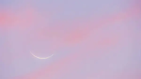 New moon at sunset. Sky of pink and bluish tones with the profile of the new moon in the background.