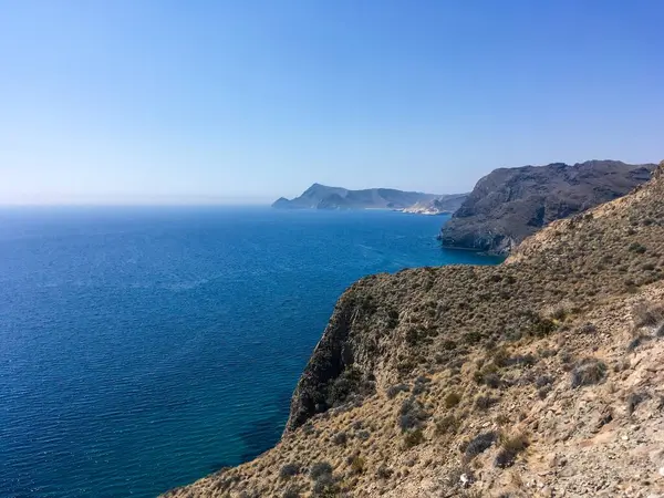 Almerya 'da güneşli bir yaz gününde kayalık ve kayalık bir sahil. Ufukta Cabo de Gata, Endülüs, İspanya 'daki Kara Tepe ve La Polacra pelerinini görebilirsiniz..