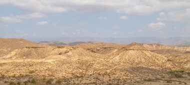 Tabernas, Almeria, İspanya civarındaki çöl manzarası. Tepelerden ve küçük bitki örtüsü olan derin vadilerden oluşan çorak bir arazi. Bulutlu yaz günü.
