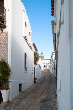Küçük bir Endülüs kasabasının beyaz yıkanmış sokaklarında beyaz evler. Sanlucar de Guadiana 'daki dar Fria Caddesi. Arkadaki Çiçeklerin Leydisi kilisesinin çan kulesi. İspanya. 2019.