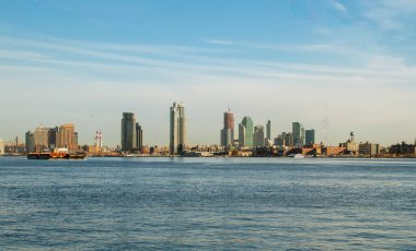 Long Island gökdelenleri ve New York, ABD 'deki East River Promenade' den East River. Şafak vakti bir mavna yelkenlisinin ilk ışıklarıyla ve arka planda binalar ve gökdelenler..