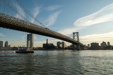 New York, Birleşik Devletler. 09 11 2019. Yolcularla birlikte Doğu Nehri 'ne giden feribot. Williamsburg Köprüsü 'nün altından geçerken ve arka planda en ikonik gökdelenler onun yanında yer alır..