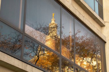 Reflection in a window of the David N. Dinkins Municipal Building in Manhattan, New York, USA. Reflection of a tree in autumn and details of the dome, the golden statue of Civic Fame. clipart