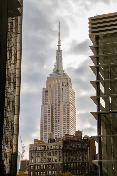 New York City ufuk çizgisinin alçak açılı görüntüsü, arkasında bulutlu bir gökyüzü var. 6. caddeden görülen ikonik Empire State Binası diğer gökdelenlerin arasında duruyor..