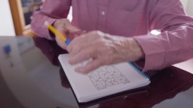 Sudoku bulmaca kitabına yazmak için kalem yardımıyla artriti olan yaşlı adamı kapatıyoruz.