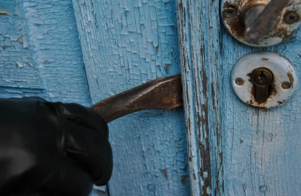 a hand in a black glove breaks the lock of an old door with a crowbar. burglar opens the door