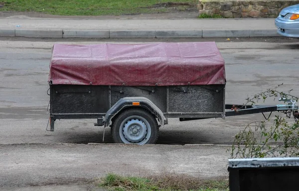 There is a car trailer covered with an awning on the side of the road. cargo trailer for a passenger car with a protective awning.