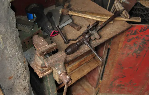 Workplace of a foreman in an old workshop. old bench vice and hand drill. old tools on a dark photo.