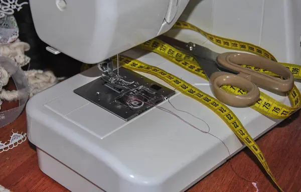 Dikiş makinesinin bir kısmını kapatıyorum. Dikiş makinesi için iğne ve bir santimetre ile makas. Terzinin işyeri..