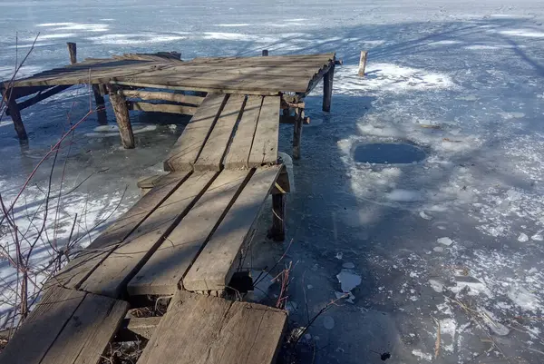 Kışın donmuş bir nehirde eski ahşap iskele.
