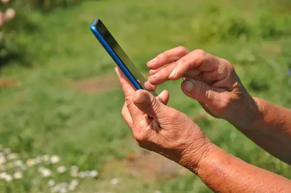 Akıllı telefon yaşlı bir kadının elinde, yakın plan. Yaşlı bir kadın cep telefonu kullanır..