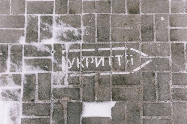 Tahliye için hava saldırısı sireninin çalması durumunda hangi yöne hareket edileceğini gösteren bir ok çizimiyle kaldırıma yazılmış Ukraynaca bir yazı.