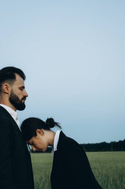 Yeşil bir tarlanın ortasında klasik takım elbiseli genç bir çift fotoğraf çekiminde. Birbirine aşık iki insan arasındaki ilişki kavramı.