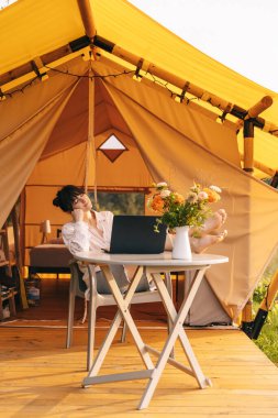 Mutlu kız tatilde dinleniyor. Kamp yapan genç bayan kamp çadırında oturuyor. Genç beyaz kadın, metin okuyor ve defter üzerinde çalışıyor.