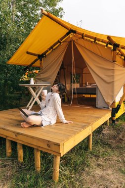 Mutlu kız tatilde dinleniyor. Kamp yapan genç bayan kamp çadırında oturuyor. Genç beyaz kadın, metin okuyor ve defter üzerinde çalışıyor.