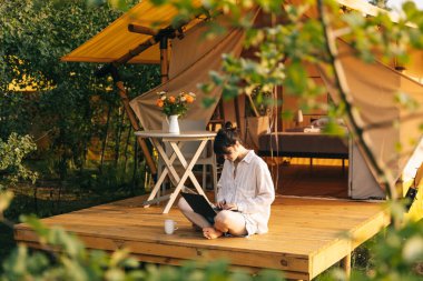 Haftasonu işi, kadın güne bir dizüstü bilgisayarla başlarken turistler için bir çadır yakınında oturuyor.