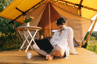 Haftasonu işi, kadın güne bir dizüstü bilgisayarla başlarken turistler için bir çadır yakınında oturuyor.