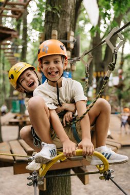 Küçük gülümseyen bir kız ve oğlan yaz halat parkında ip kemerine tırmanıyor engelleri aşıyor